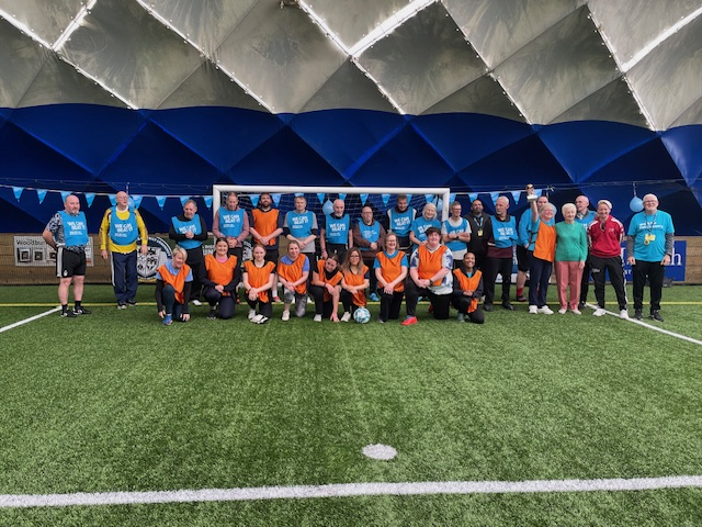 Two teams of a walking football match posing in front of the goal