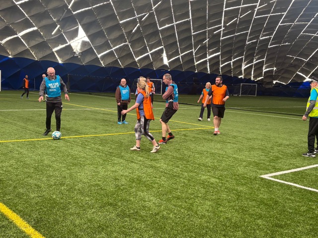 Another view of a walking football game and people wearing blue and orange bibs