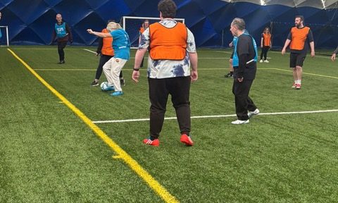 Walking Football 2026 A walking football game with people wearing orange and blue bibs