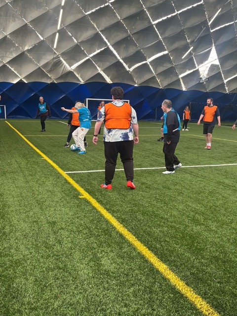 A walking football game with people wearing orange and blue bibs