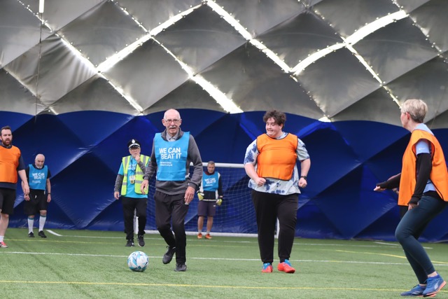 People with blue and orange bibs playing walking football